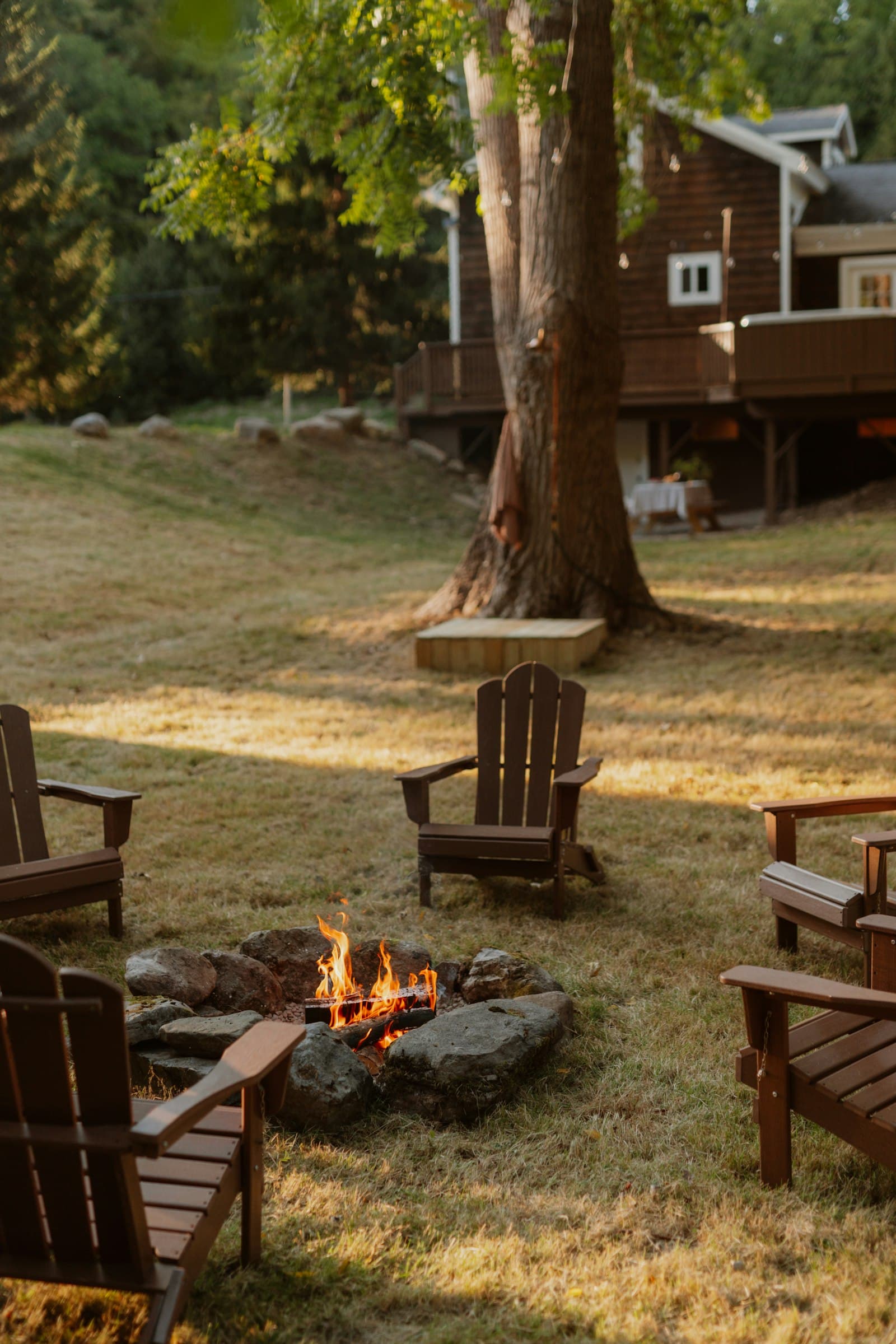 Adirondack chairs around a fire pit on a green lawn at golden hour