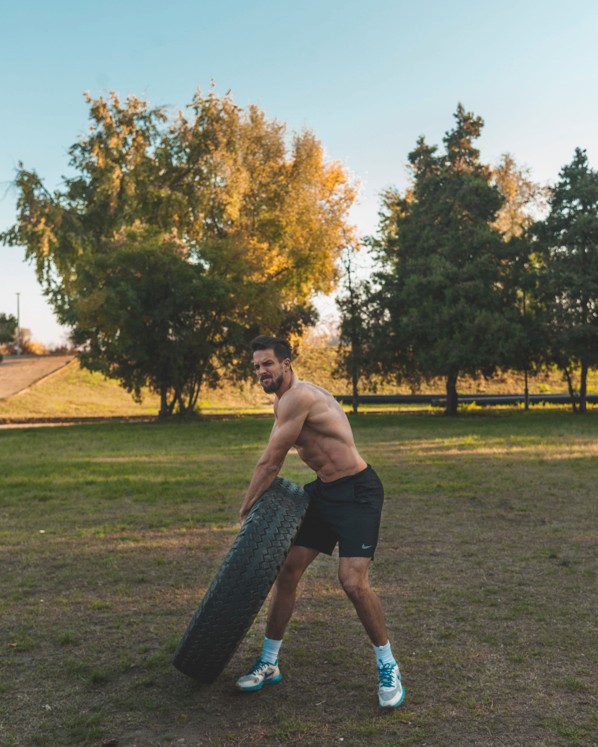 Bearded athlete flipping a heavy tire on a grass lawn at golden hour