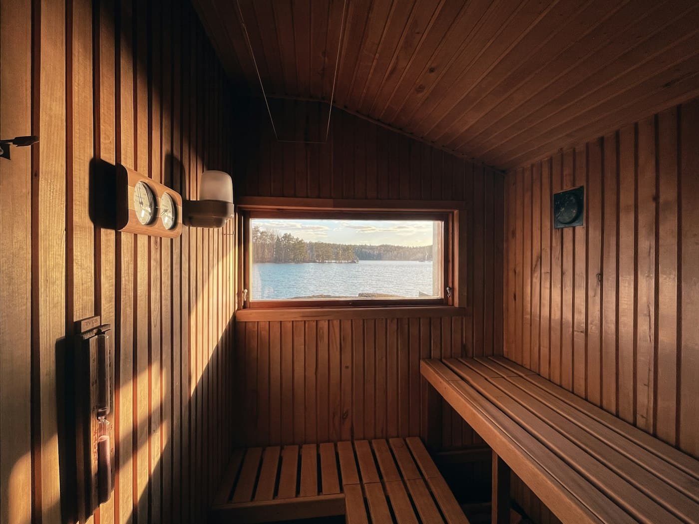 Warm cedar sauna lit by sunlight through a wide window with a view outdoors